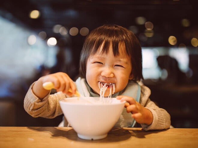 toddler eating noodles from a bowl at a restaurant toddler eating noodles from a bowl at a restaurant