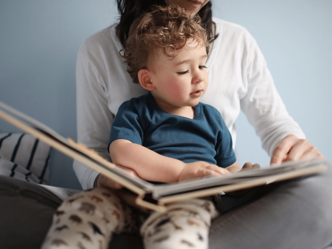 Toddler reading a book on mums lap Toddler reading a book on mums lap
