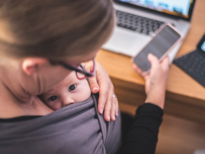 Woman on the phone with baby in grey carrier Woman on the phone with baby in grey carrier