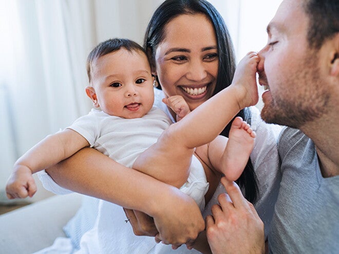 Woman holding her baby while they play with mans face with feet Woman holding her baby while they play with mans face with feet