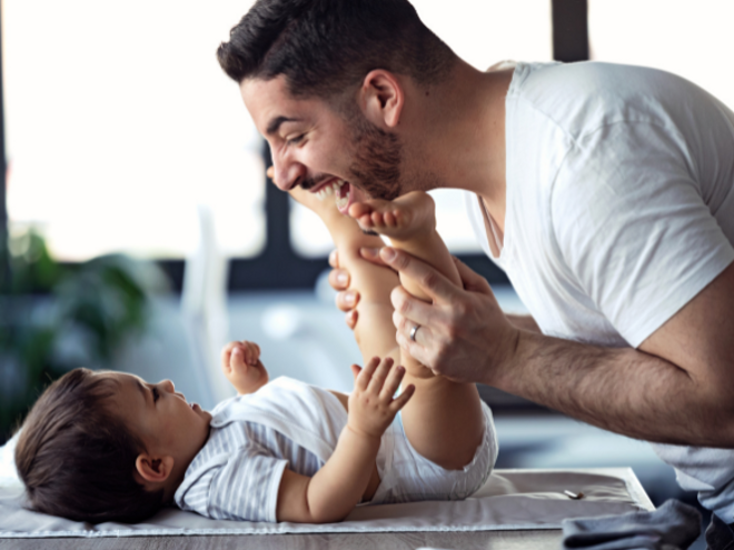Baby laying down and father making the baby laugh leaning over Baby laying down and father making the baby laugh leaning over