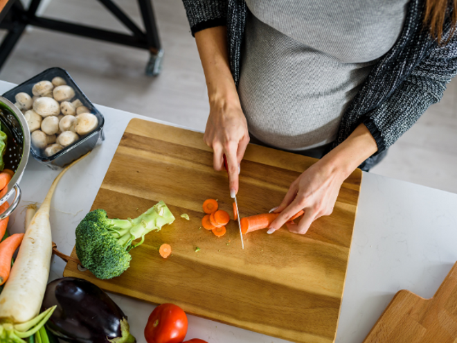 pregnant woman cutting carrot on a wooden chopping board pregnant woman cutting carrot on a wooden chopping board