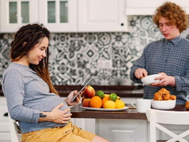 Pregnant woman looking at iPad with man in the kitchen Pregnant woman looking at iPad with man in the kitchen