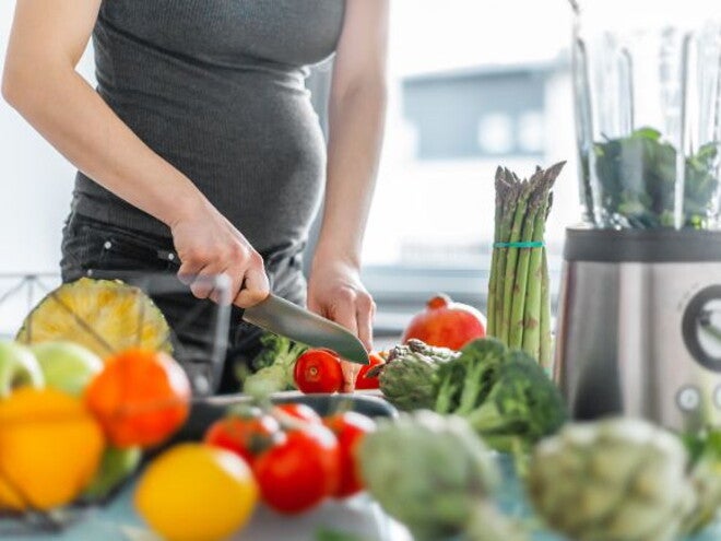 Pregnant woman in dark top cutting vegetables Pregnant woman in dark top cutting vegetables
