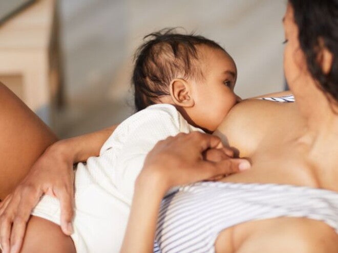 Mother in striped top breastfeeding her baby in a white onesie Mother in striped top breastfeeding her baby in a white onesie