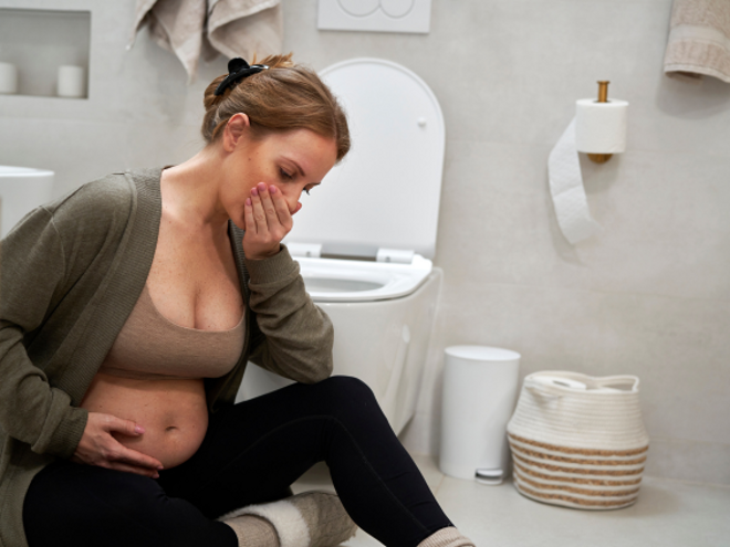 Pregnant lady sitting on the ground in a bathroom with her hand over her mouth Pregnant lady sitting on the ground in a bathroom with her hand over her mouth