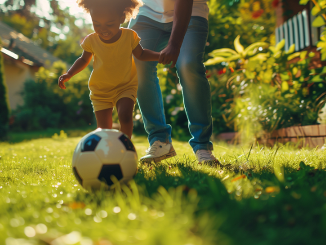 Toddler girl kicking the soccer ball while holding parents hand Toddler girl kicking the soccer ball while holding parents hand