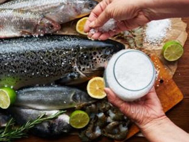 Raw fish being seasoned with salt.