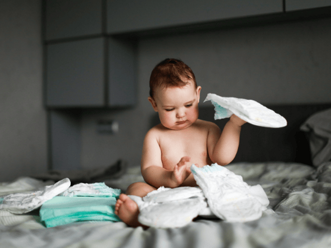 Toddler Diarrhoea Baby sitting on bed playing with nappies