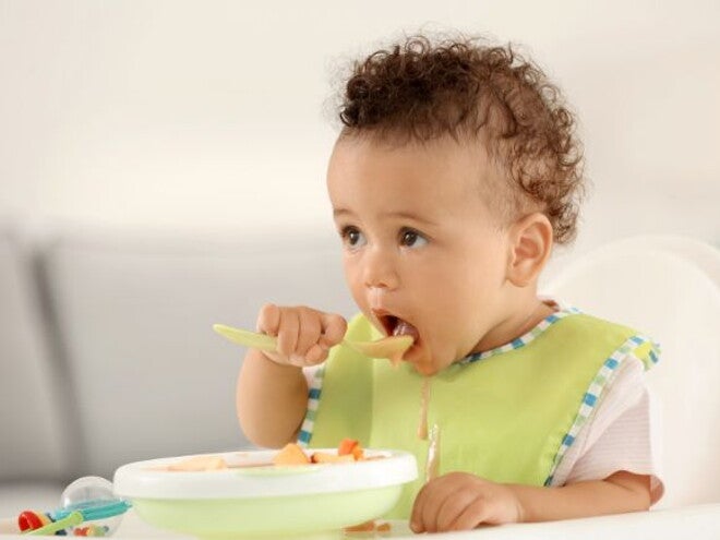 baby eating with bib on with a spoon and bowl baby eating with bib on with a spoon and bowl