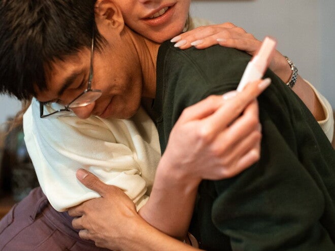 man in green shirt and woman in white shirt hugging with a pregnancy stick in hand man in green shirt and woman in white shirt hugging with a pregnancy stick in hand