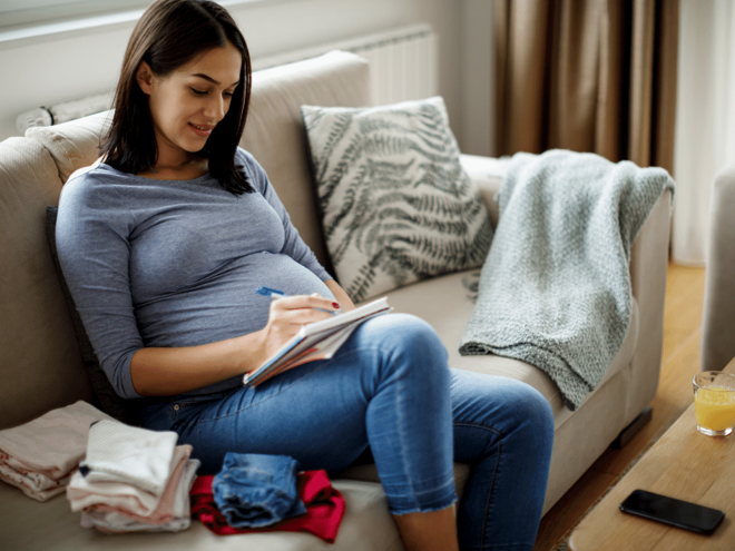 pregnant woman on couch writing on a notepad pregnant woman on couch writing on a notepad