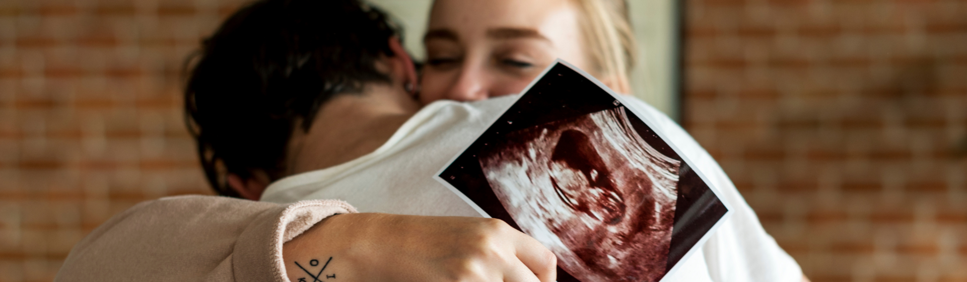 Woman hugging partner with ultrasound image in her hand Woman hugging partner with ultrasound image in her hand
